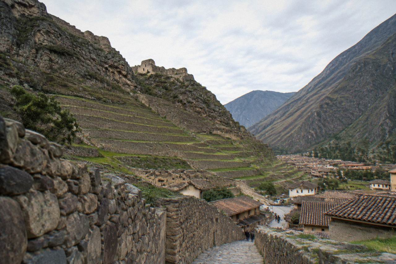 Steep farming terraces rising above the tile roofs of a small valley town with green hills behind