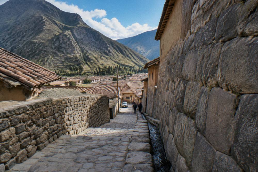 A narrow stone street with fitted Inca walls and a water channel running beside the paving
