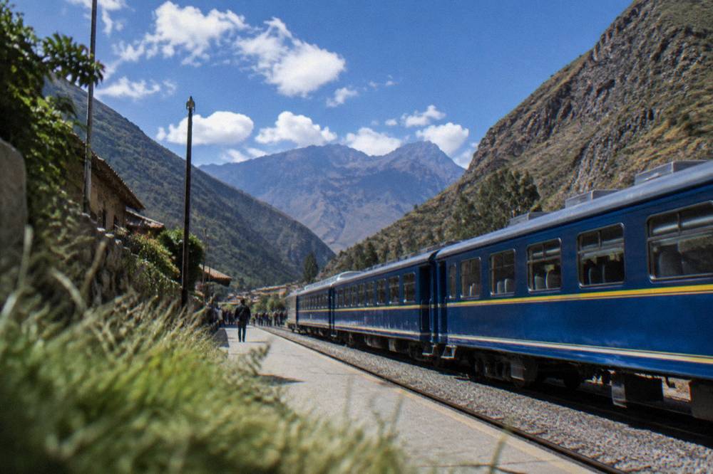 A rail platform in a valley town with a waiting train and mountains behind it