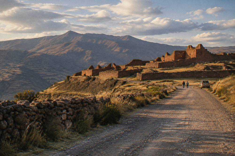 A dry gravel road leading toward stone ruins under a wide Andean sky