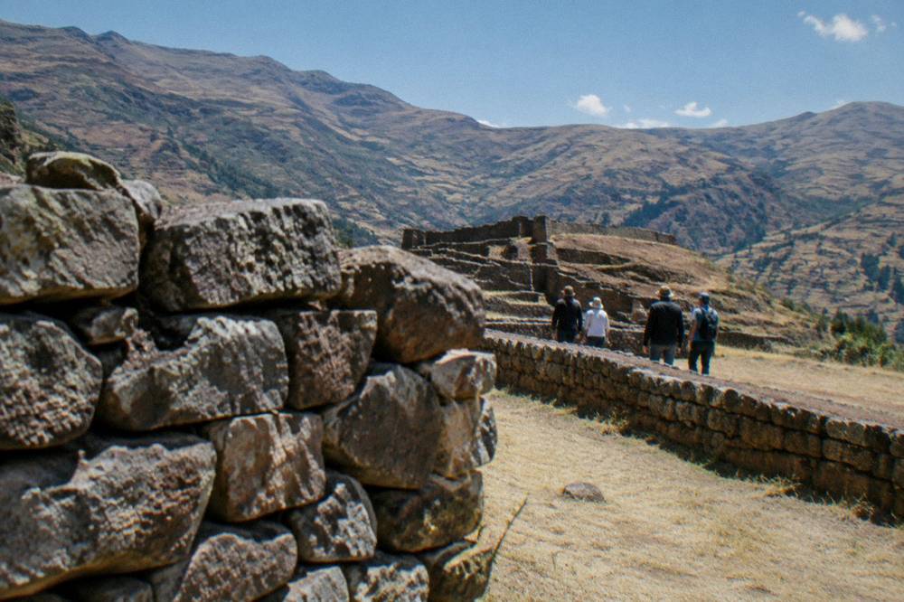 A small group of visitors walking along a low stone wall in bright daylight