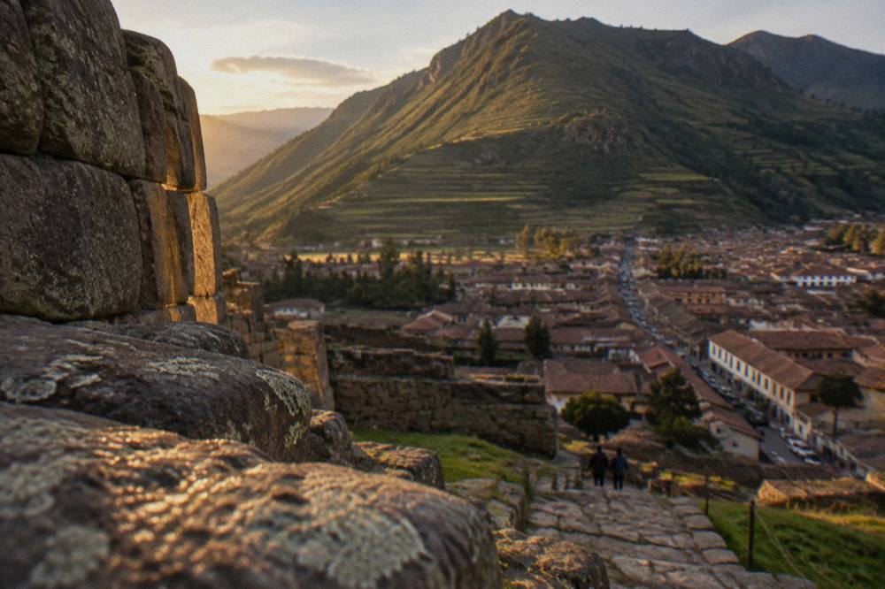 Red-roofed town buildings below a green mountain ridge with terraced fields