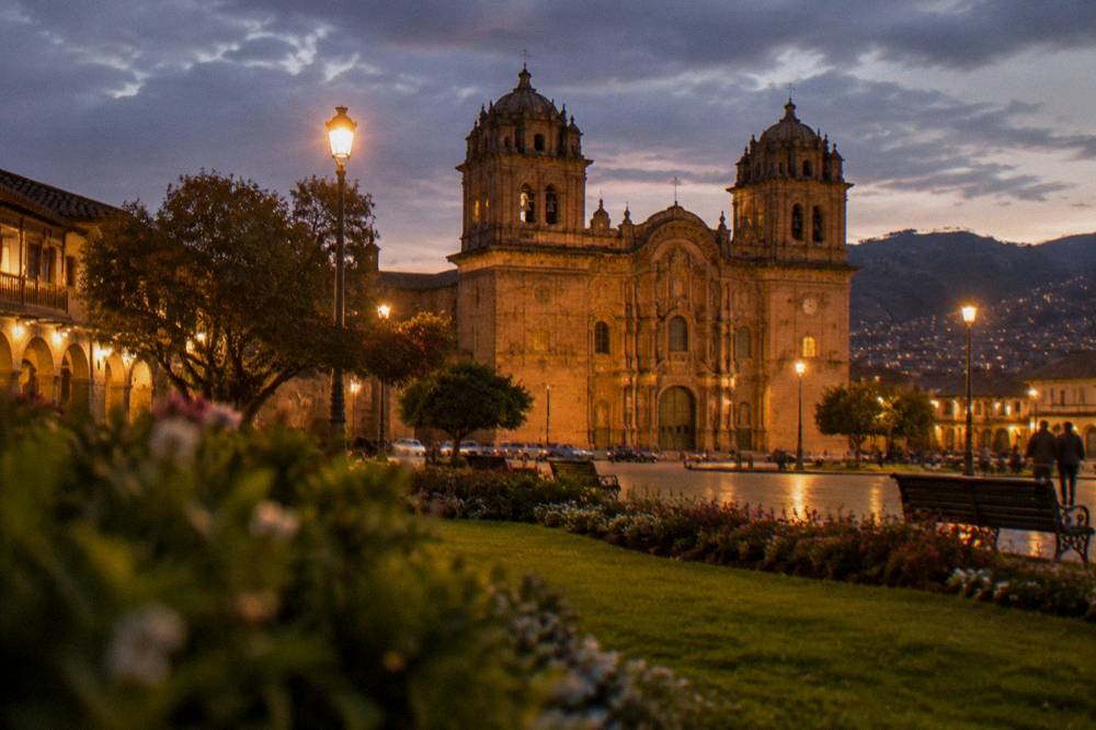 The cathedral facade and bell towers seen from the gardens in the square at dusk