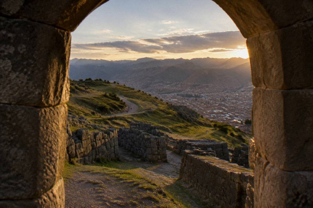 A winding road and grassy hills above the rooftops of Cusco with mountains on the horizon