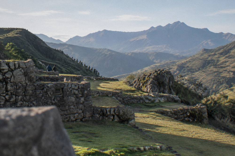 A quiet stone terrace at an Inca site with green hills and distant mountains beyond