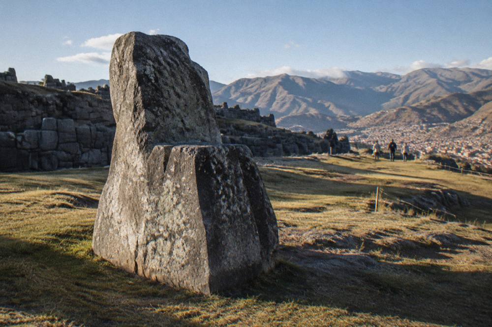 Open hillside with a carved stone monolith and the Andean skyline beyond