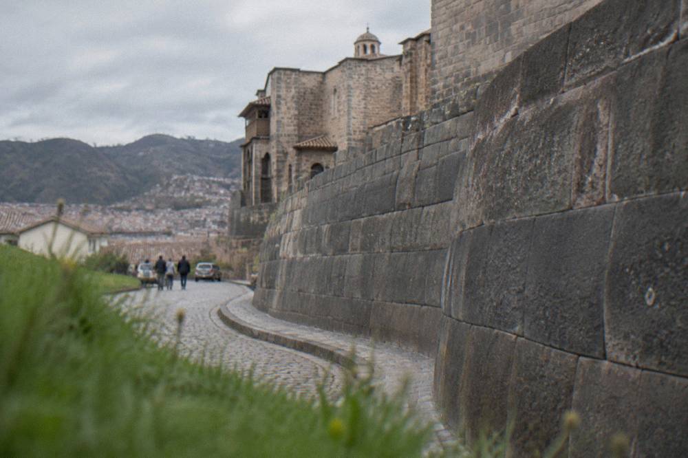 A sunlit colonial cloister with stone arches beside an ancient Inca wall
