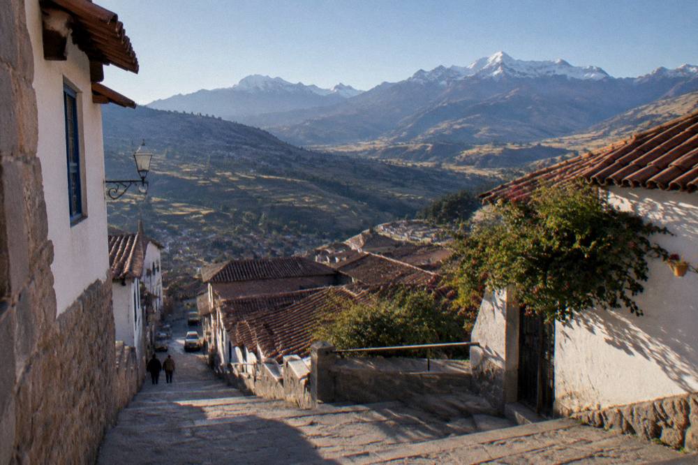 An Andean valley landscape with terraced fields and distant snow peaks under a clear sky
