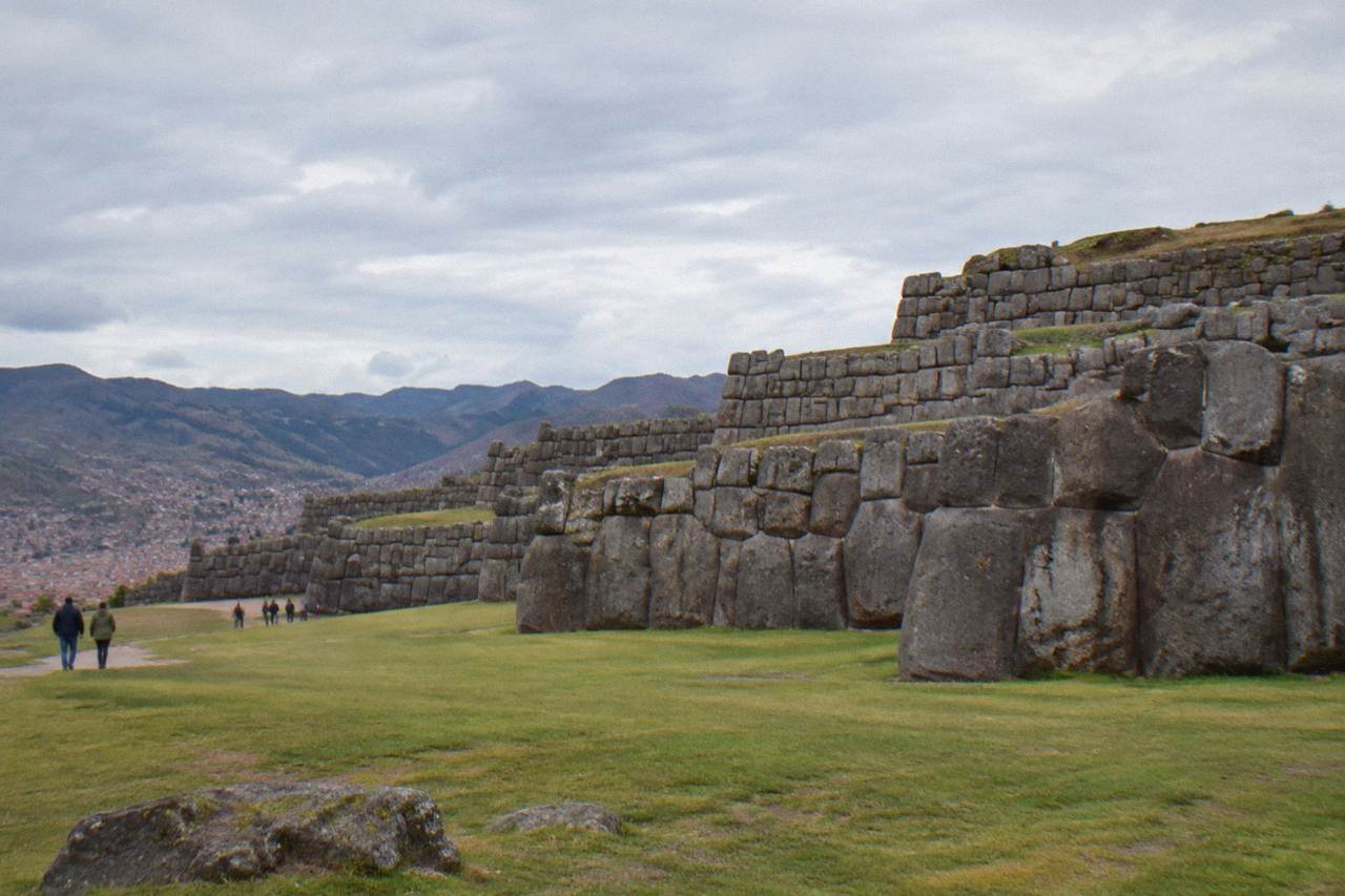 Stepped stone terraces rising above a grassed esplanade with the rooftops of Cusco in the valley below