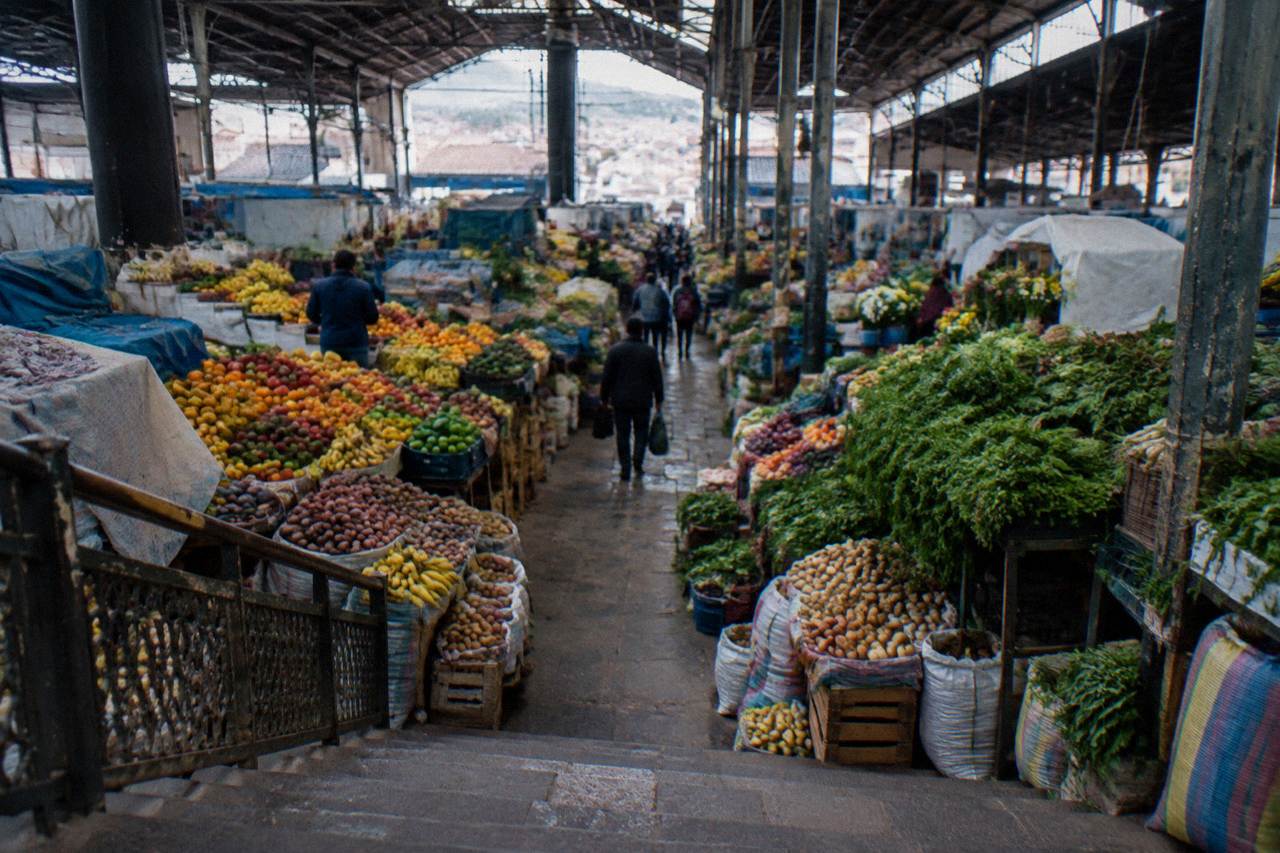 Rows of fresh fruit and vegetables stacked on stalls under the roof of a covered market hall