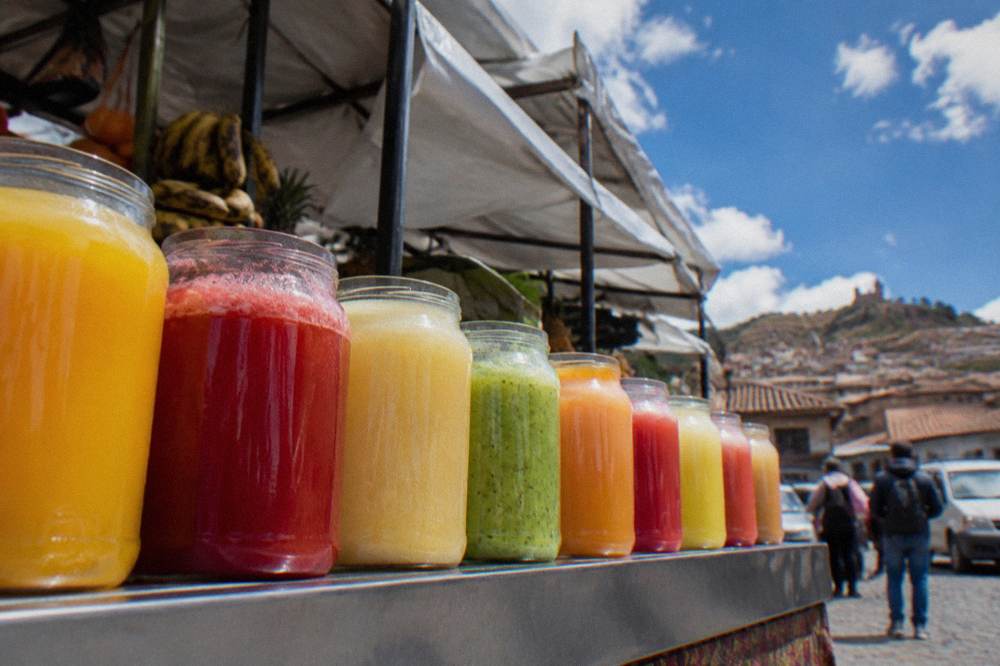 Glass jars of colourful fresh fruit juices lined up along a market counter