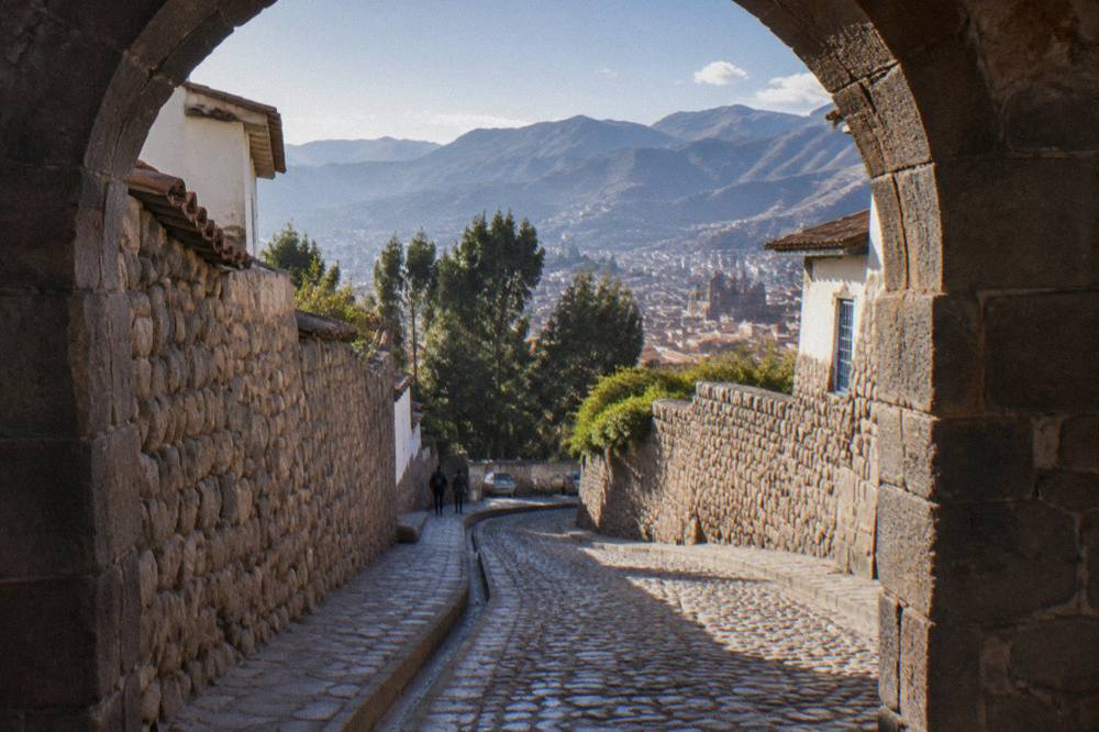 A steep cobbled lane in Cusco curving down between old stone walls toward trees