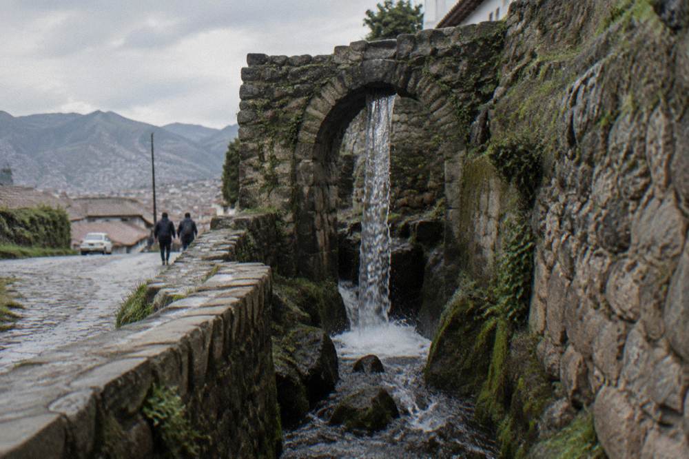 A thin waterfall dropping from a stone arch into a rocky channel after rain