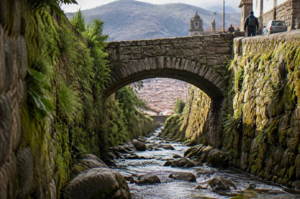 The stone arch of the aqueduct seen from the stream bed with sunlight on the mossy walls