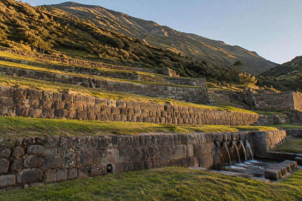 Wide stone farming terraces of Tipon stepping down a green Andean hillside under a clear sky