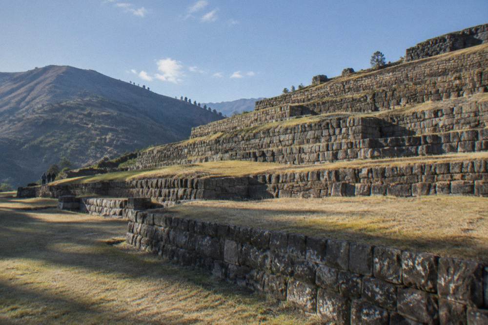 Stepped stone terrace walls rising up a slope at Tipon with dry grass on the levels