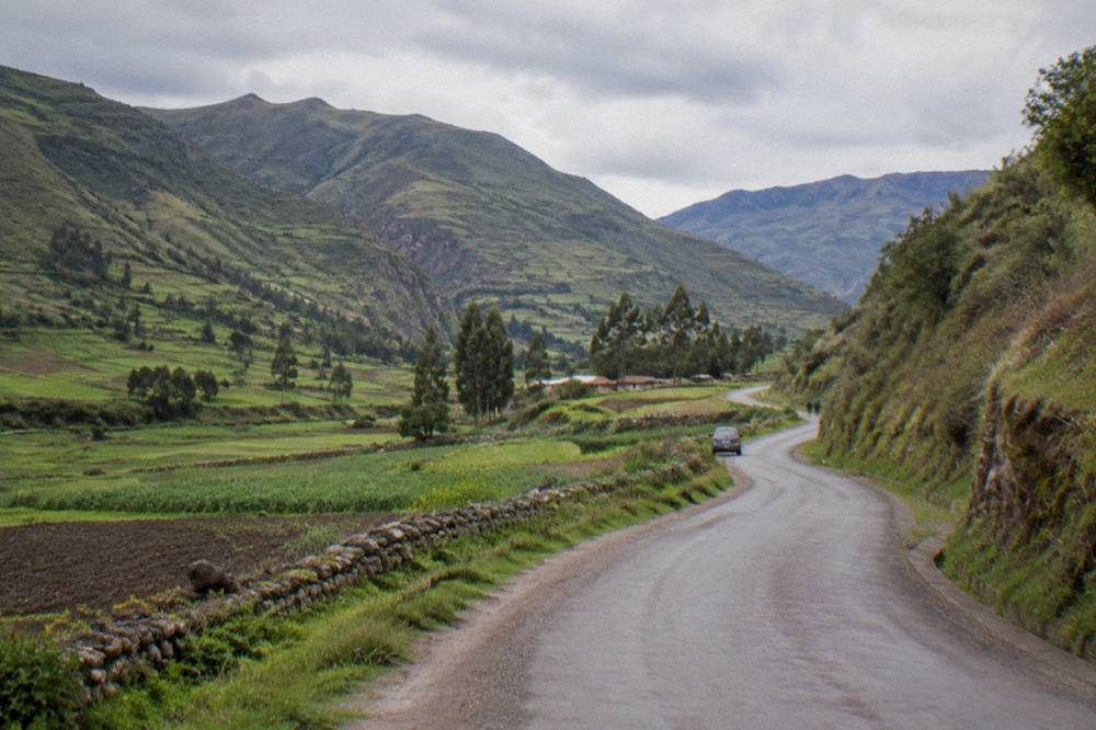 A rural road winding through the green South Valley of Cusco with farmland on either side