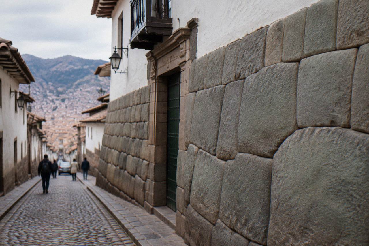 A tall stone wall of large fitted blocks on a narrow sloping street in Cusco with a many cornered polygonal block at its centre