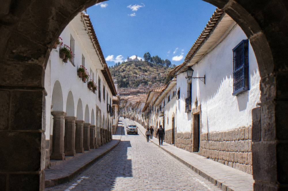 A whitewashed colonial arcade and stone street climbing toward a hillside quarter under a blue sky