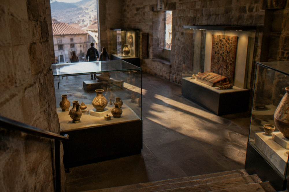 A museum hall with glass cases holding pre-Columbian ceramics and textiles lit softly against stone walls