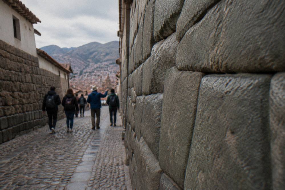 A small group of walkers with a guide listening on a narrow stone street beneath old walls