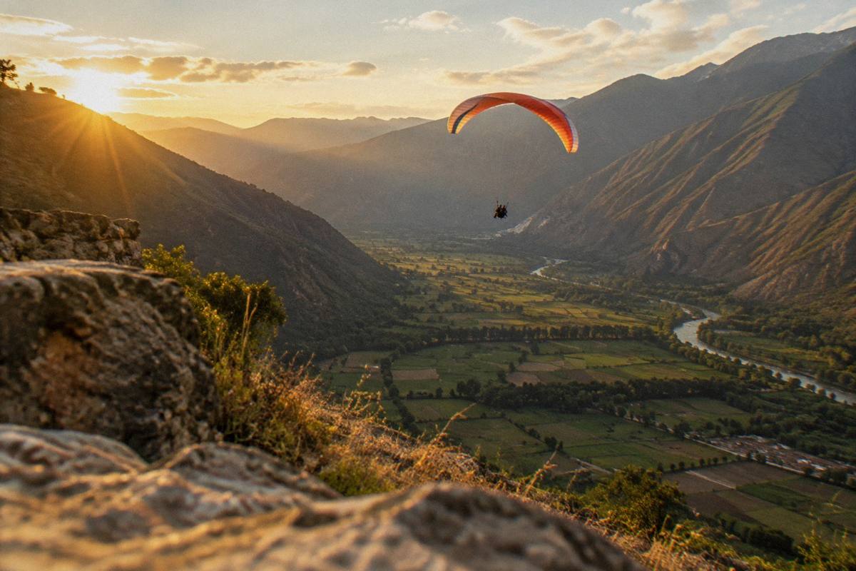 A single tandem paraglider canopy high above the green Sacred Valley, fields and the river far below, Urubamba