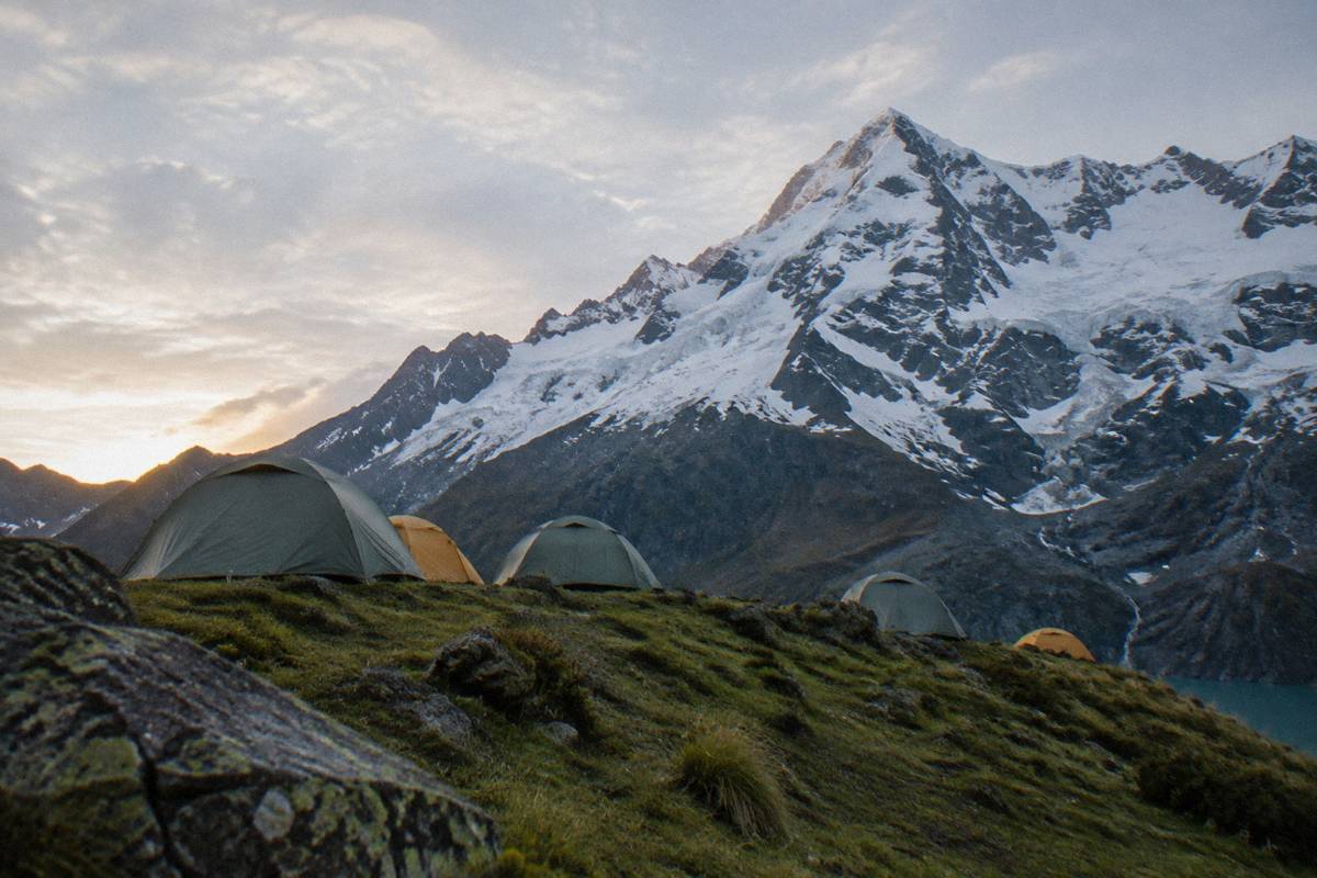 A high mountain camp of small round tents on a grassy ridge below a snow peak at dawn, nobody visible, Humantay Lake