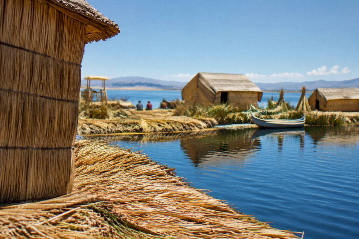Golden reed platforms and reed houses of the Uros floating islands on calm blue Lake Titicaca, the far shore low on the horizon