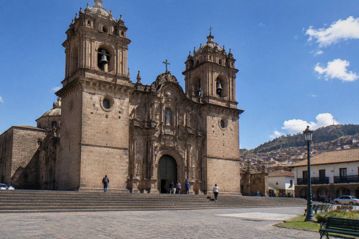 The ornate stone front of the Jesuit church beside the Plaza de Armas, twin towers and a carved portal, a few distant visitors on the steps, Church of La Compania de Jesus