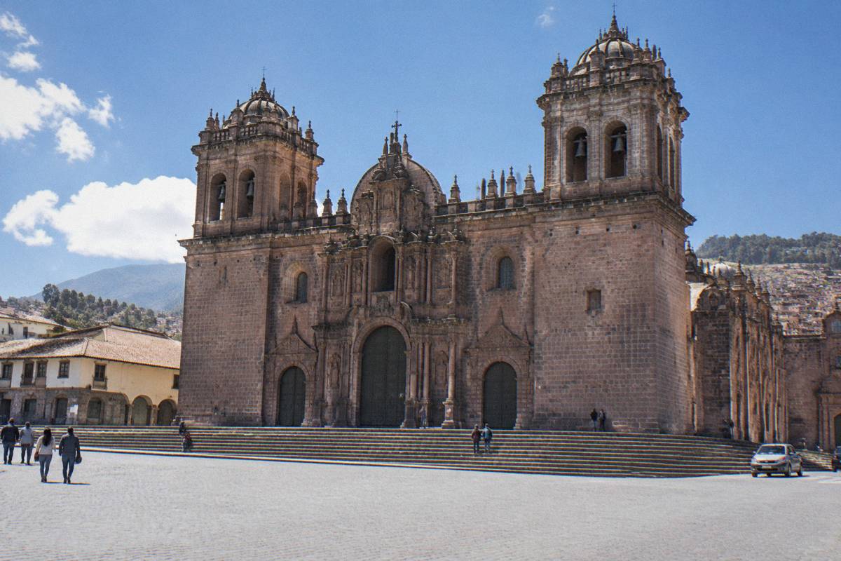 The stone front of Cusco Cathedral with its twin bell towers and wide steps, a few small distant visitors