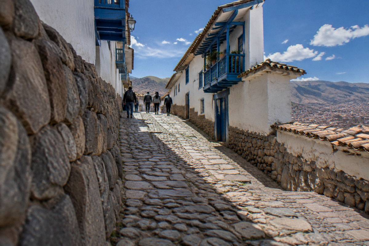 A steep cobbled San Blas lane with whitewashed walls and blue balconies, a small group of walkers from behind near the top