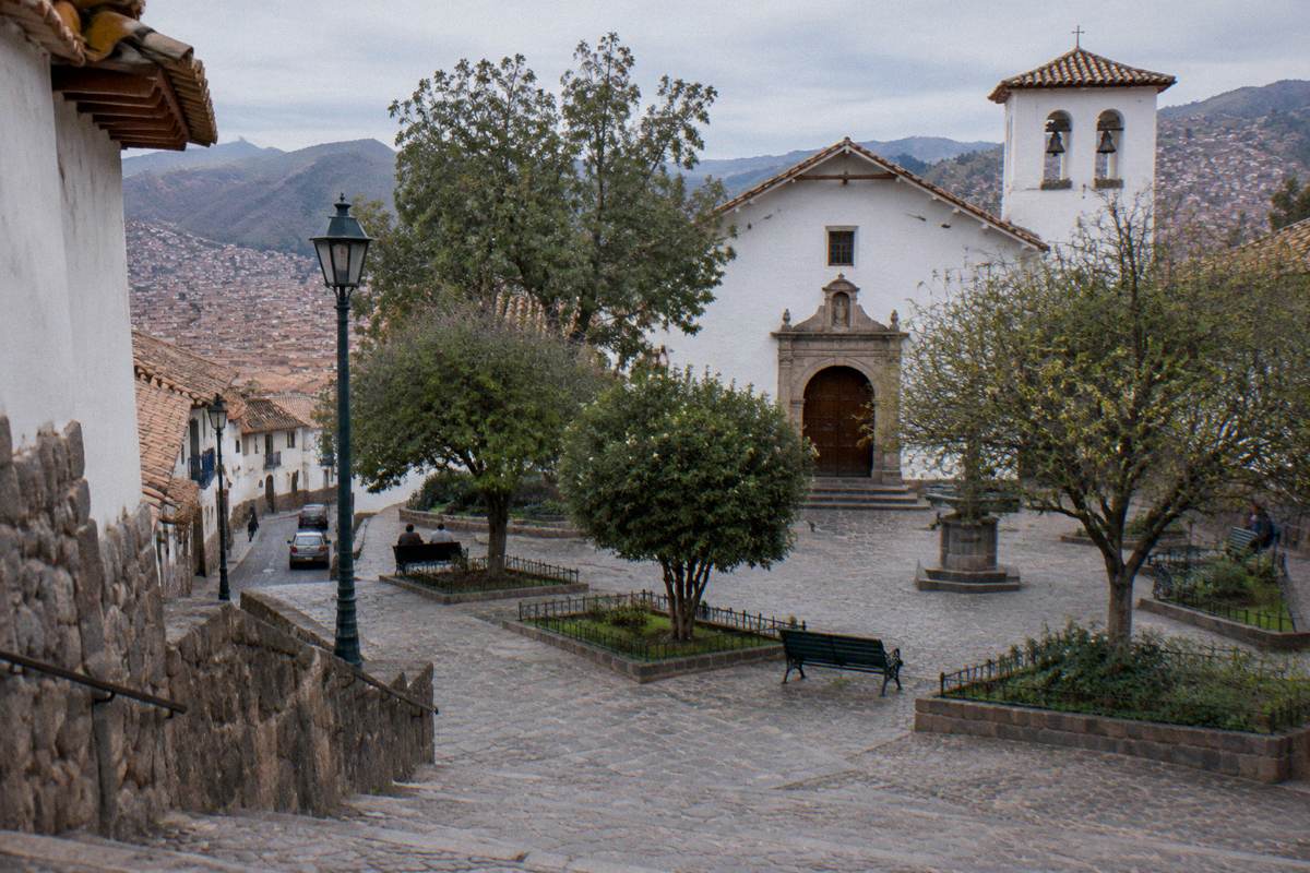 The small plaza of San Blas with a plain whitewashed church front, trees and benches, quiet morning light