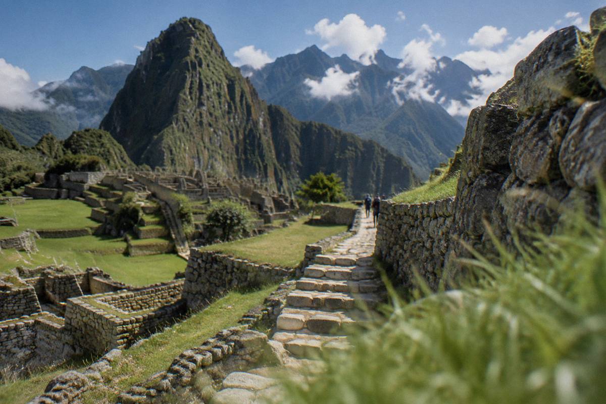 A stepped stone staircase between terraces running through the Machu Picchu ruins, a long narrow path ahead, cloud and green peaks beyond