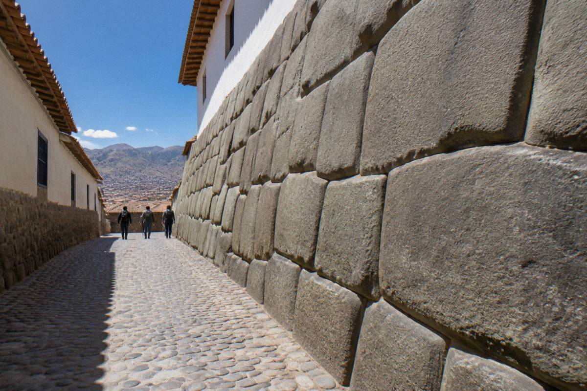 Looking along the narrow cobbled lane beside the large fitted Inca wall, a small group of walkers far ahead seen from behind