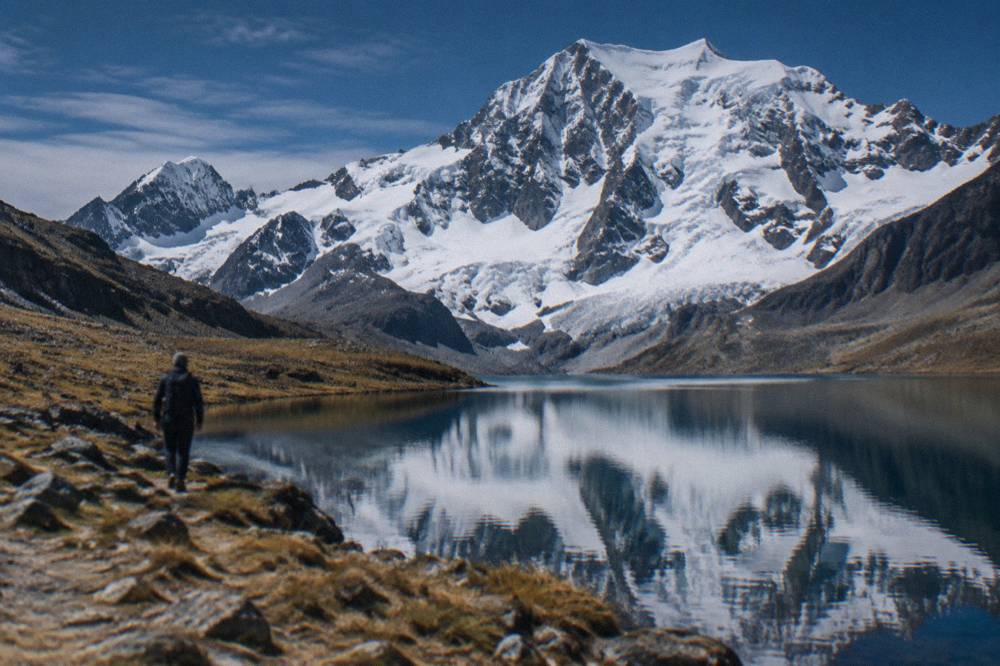 Icy lake water reflecting a snow-covered mountain face under a deep blue sky