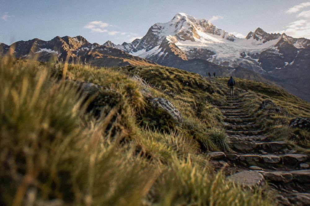 Stone steps climbing a grassy ridge toward a snowline