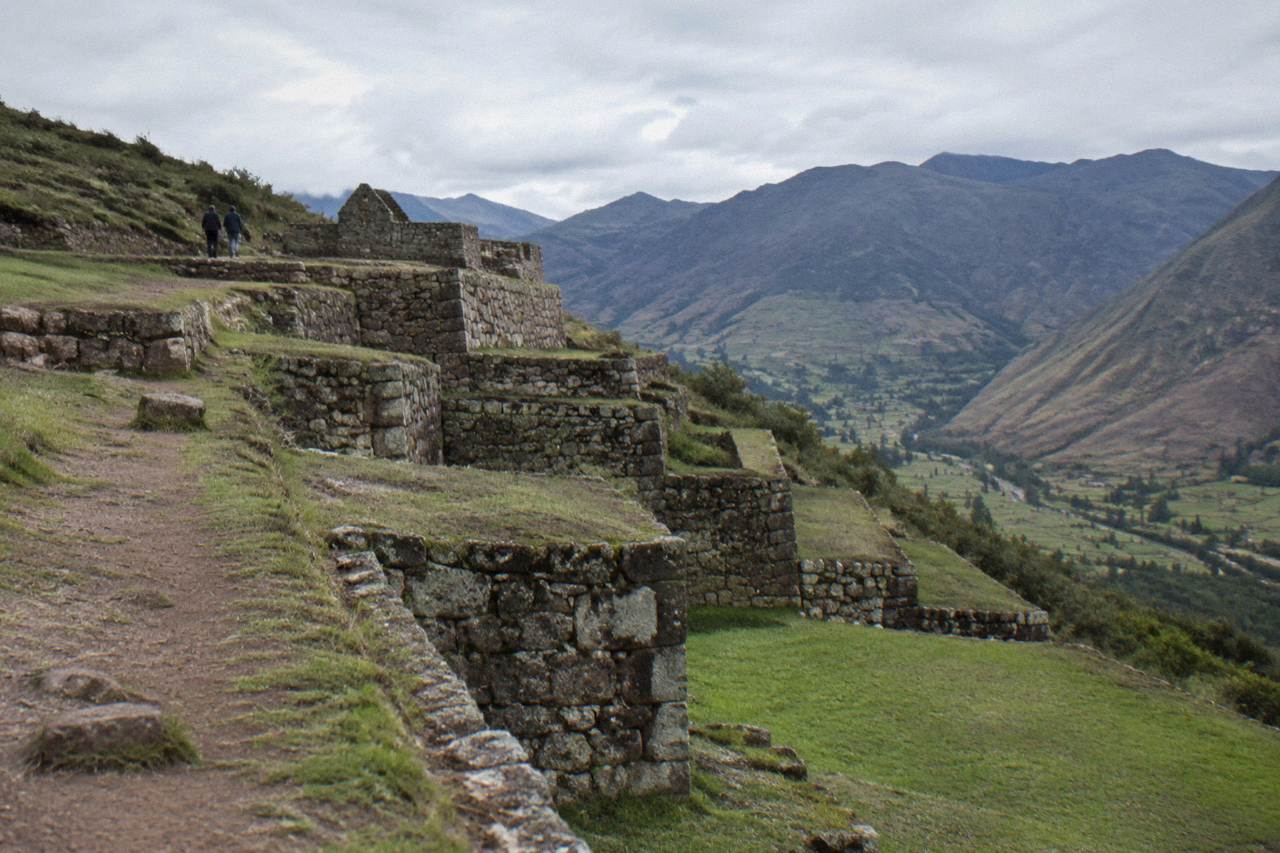 Stone terraces of an Inca archaeological site on a green ridge above a valley in the Peruvian Andes