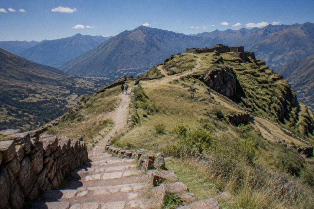 Walking path along a grassy Andean ridge with mountains in the distance under a blue sky