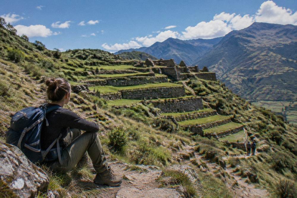 Hiker in outdoor clothing resting on a hillside path above green agricultural terraces