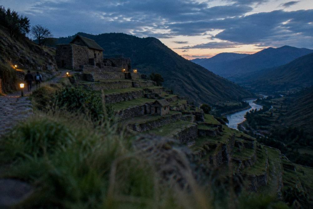 Terraced hillside above a river valley with small stone structures under an afternoon sky