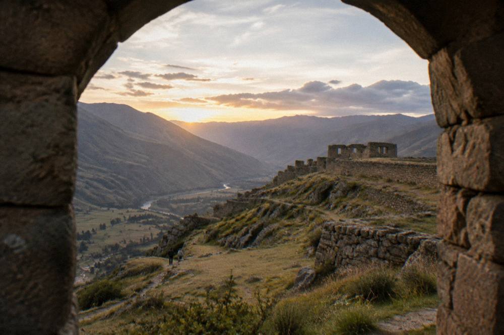 Wide view of an Andean valley at golden hour with a stone ruin on a ridge in the distance