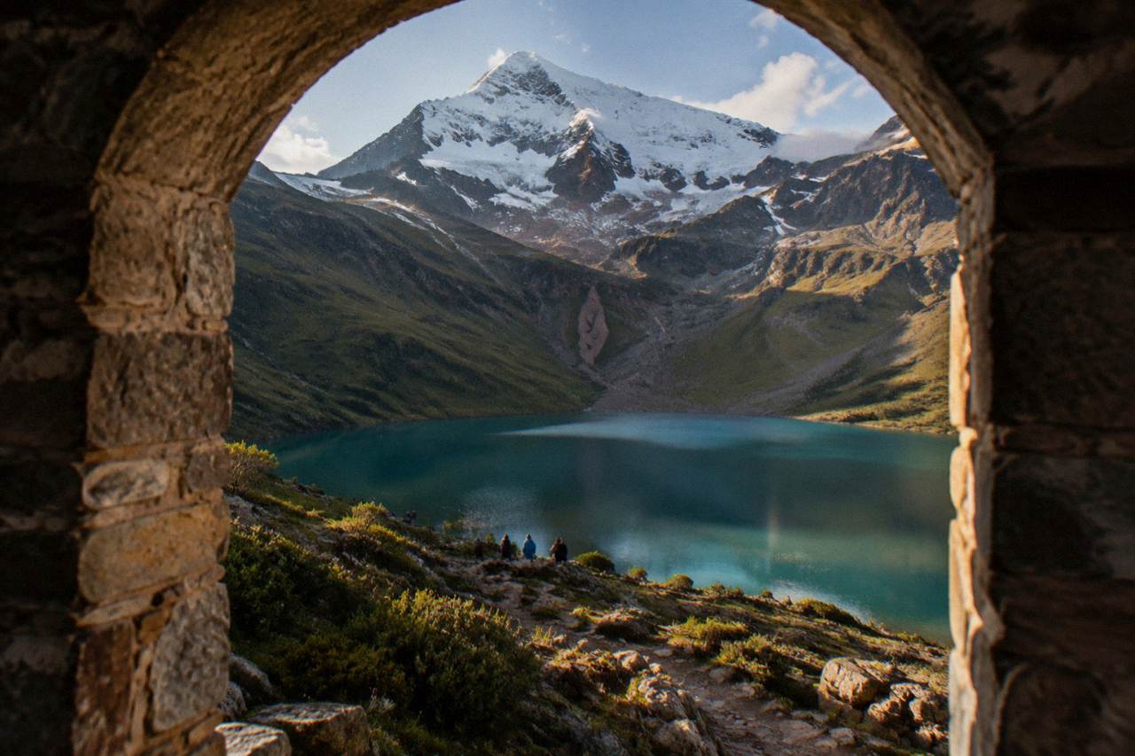 A turquoise mountain lake held in a bowl of steep grassy slopes beneath a snow-capped peak