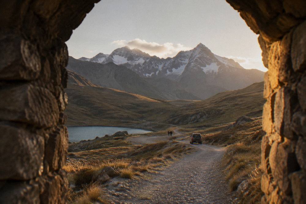 A gravel road winding through high Andean grassland toward distant snow peaks