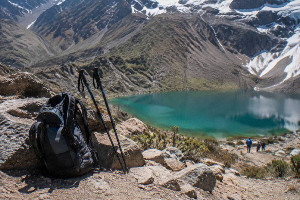 Backpacks and trekking poles resting on a high mountain trail with a lake below