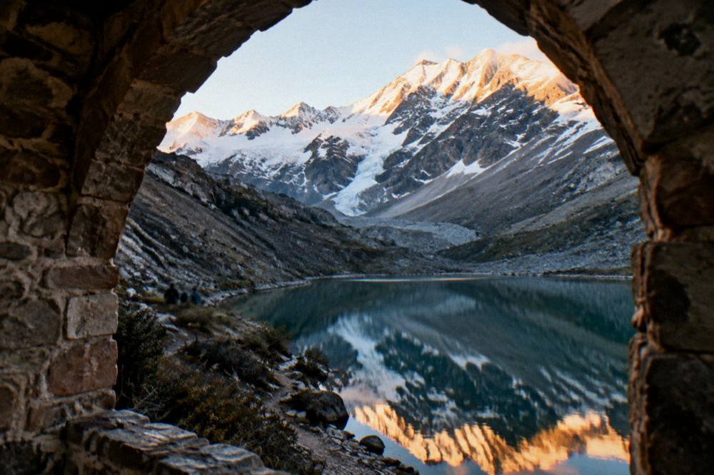 Still water of a mountain lake reflecting snow-capped peaks at sunrise
