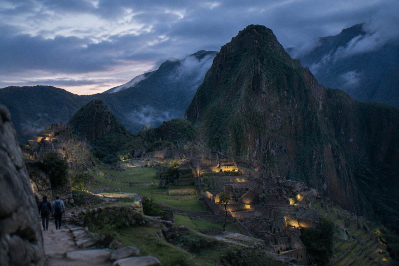 Terraced stone steps of Machu Picchu with green mountain peaks rising behind them under a cloudy sky