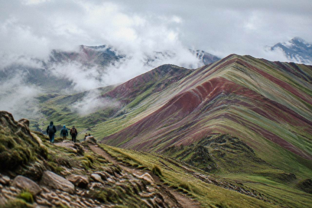 Striped red and green mountain ridges under a wide Andean sky near Cusco