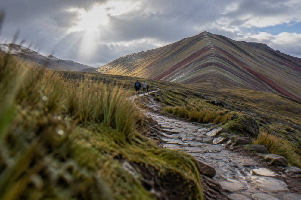 A stone path climbing gently between low Andean hills toward a striped ridge