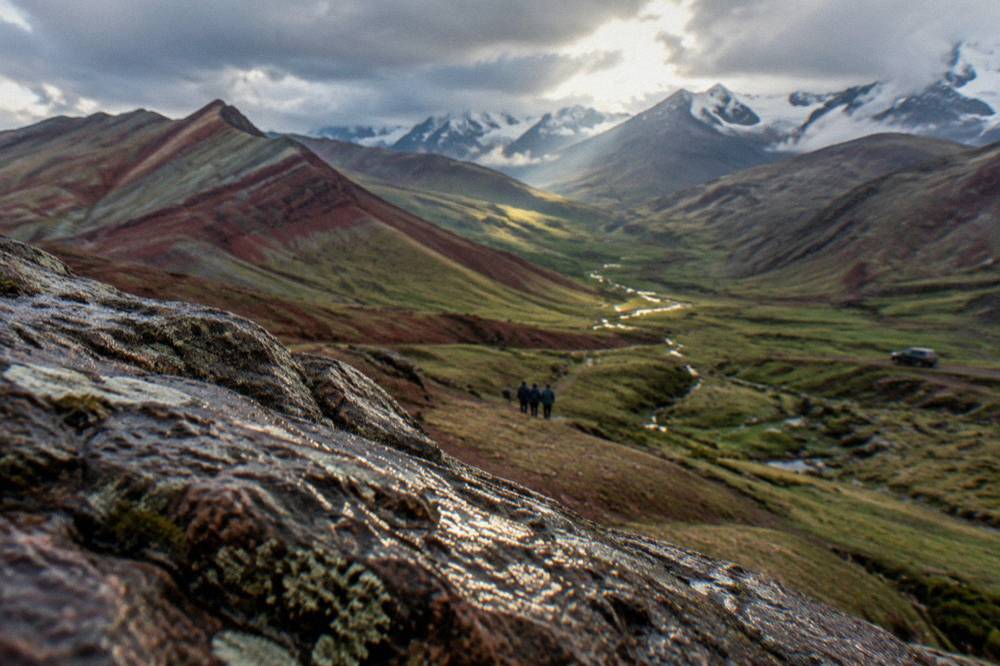 A wide valley of red rock and green pasture with distant snow peaks