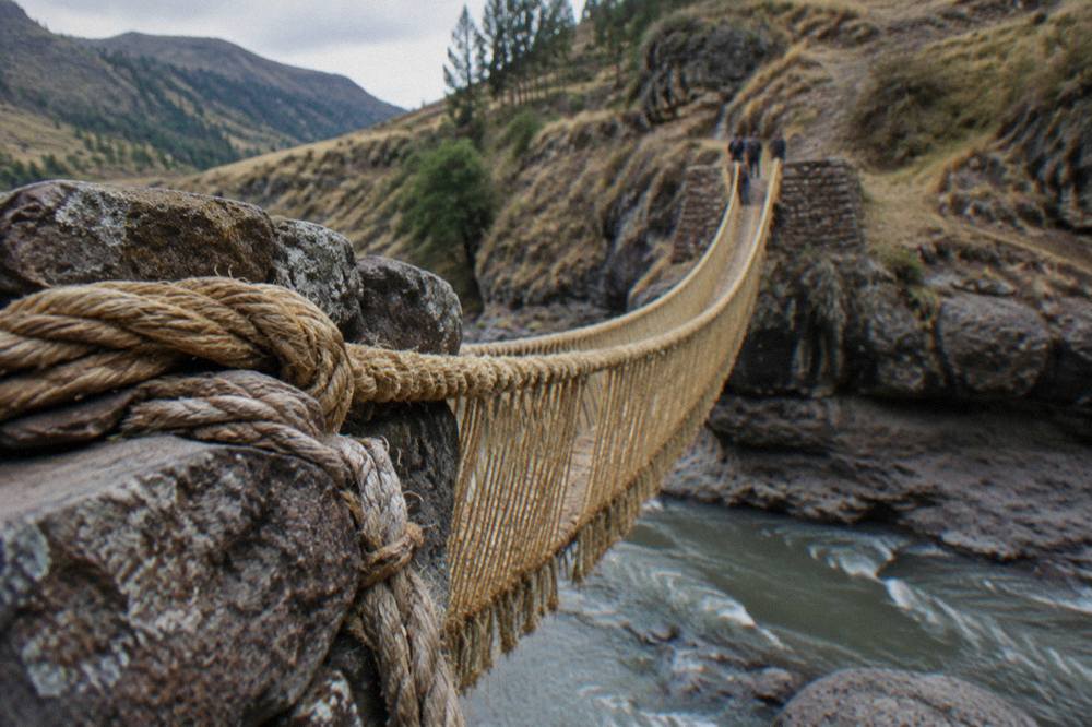 Twisted grass ropes anchored to stone abutments on a riverbank in the Andes